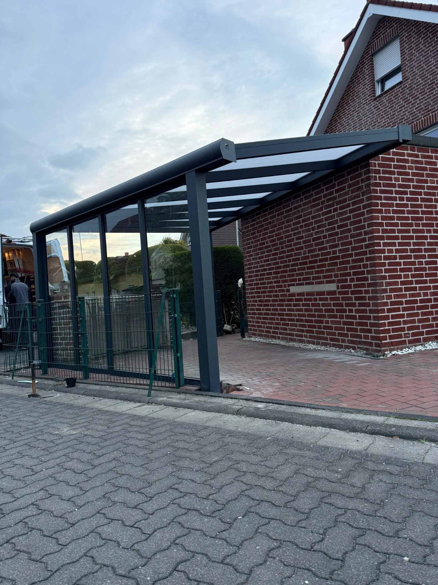 Anthrazitfarbener Carport in Trapezform mit Polycarbonatdach und Glaswand in Marl